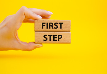 First step symbol. Wooden blocks with words First step. Beautiful yellow background. Businessman hand. Business and First step concept. Copy space.