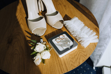 Wedding details, accessories close-up on a wooden table: bride's shoes, rings, jewelry box, garter. Photo, top view.