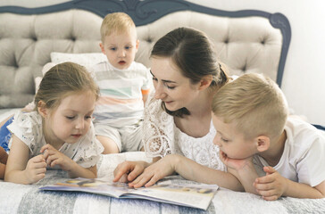 Children lie on the bed in the bedroom, mother reads a book to them.