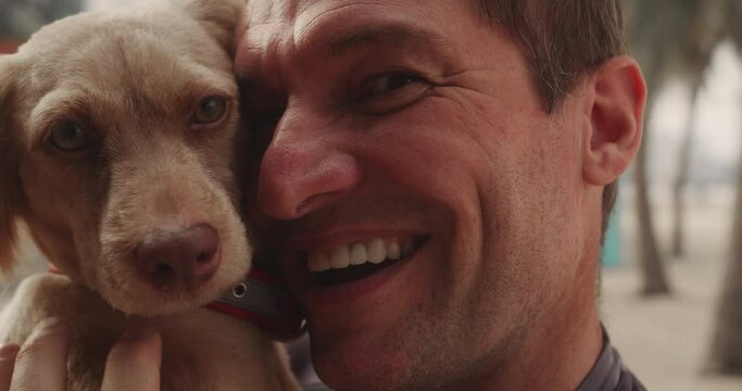 Cinematic close up shot of happy man is caressing and kissing his pedigree dog while having fun together in a street outdoors in summer. Concept: love for animals, friendship, happiness, pets