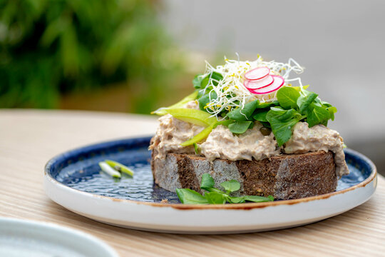 Selective focus of open sandwich in a plate with salad on top, Brown bread with mixed tuna and vegetables on table, Lunch menu dishes on outdoor terrace in summer.