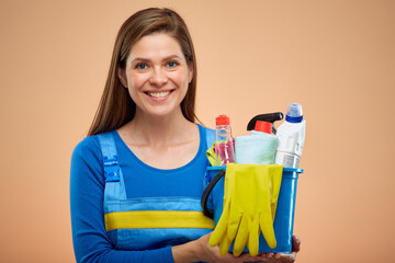 Woman cleaner in overalls holding cleaning products in bucket. isolated female housekeeper portrait on brown beige background.