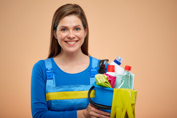 Smiling woman in overalls holding cleaning products. isolated on brown beige background.