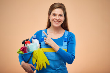 Smiling woman in overalls holding detergent and pointing finger at side up. isolated female worker...