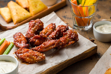 Chicken wings with blue cheese sauce and carrot and celery sticks on the board on brown wooden table macro close up