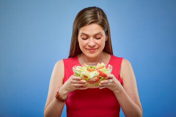 Young lady in red dress holding salad bowl and looking at him isolated portrait on blue background.