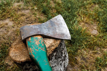 Defocus steel ax closeup. Big steel axe with wooden handle, metal ax for wood chopping. Green nature background. Forged axe it main accessory male, natural ax for survival. Out of focus