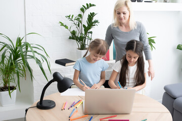 Beautiful young mother helping her daughters with homework.