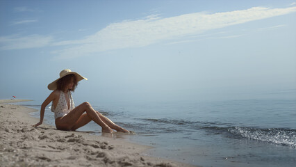 Fototapeta na wymiar Relaxed woman sitting beach sand washing legs in ocean waves. Girl sunbathing.
