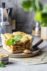 Piece of traditional apple pie with mint leave with gray tile in the back on ceramic plate, cozy rustic still life, fall baking concept