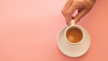 Woman's hand picking up white cup with coffee on light pink background