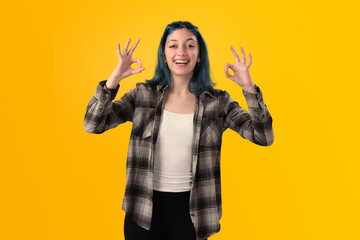 Smiling young woman student with blue hair doing positive gestures with her hands isolated over yellow background - 525699935