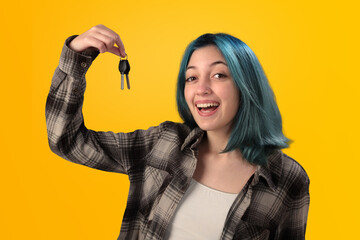 Smiling young woman student with blue hair holding keys over yellow background - 525699943