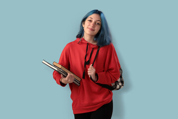 Cute young gilr student with blue hair books and a backpack over a cyan background - 525699949