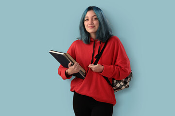 Cute young gilr student with blue hair books and a backpack over a cyan background - 525699957