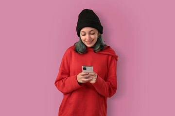 Cute young girl with blue hair using mobile phone, typing a message over pink background - 525699977