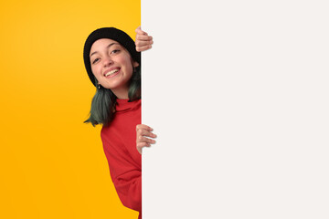 Lovely young girl holding a big blank board over yellow background - 525699995