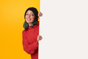 Lovely young girl holding a big blank board over yellow background - 525699997