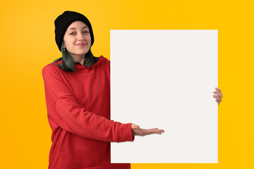 Lovely young girl holding a big blank board over yellow background - 525699999