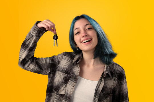 Smiling young woman student with blue hair holding keys over yellow background
