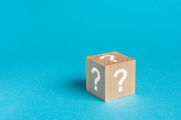 wooden toy cube with a question mark viewed high angle on a blue background with copy space in a...