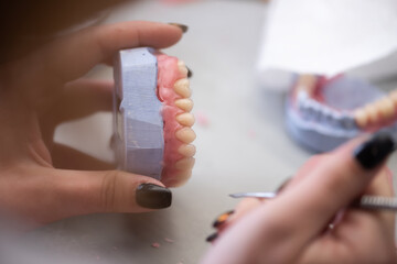 Prosthetics hands while working on the denture, false teeth, a study and a table with dental tools.