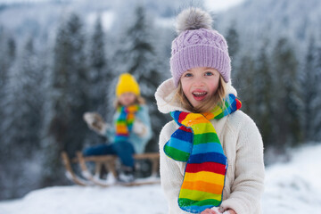 Lovely joyful girl lpaying in the winter forest. Funny excited child girl face in snow on winter outdoor. Amazed kid resting together in park with winter background. Expressive kids emotions.