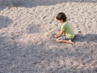 Boy is playing with gravel on modern children's playground. Developing fine motor skills and...