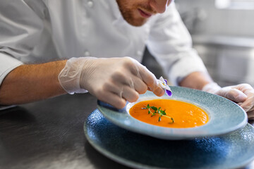 food cooking, profession and people concept - close up of male chef with flower serving plate of pumpkin cream soup at restaurant kitchen