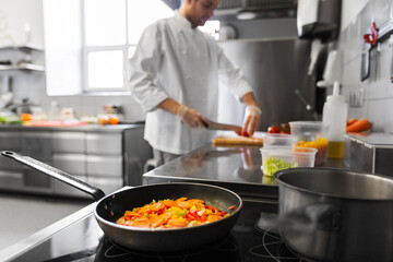 cooking food, profession and people concept - close up of frying pan with stewing vegetables and male chef at restaurant kitchen