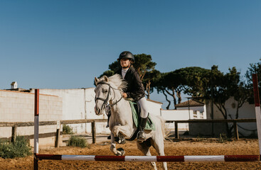 12-year-old girl riding a white pony jumps an obstacle at a riding school