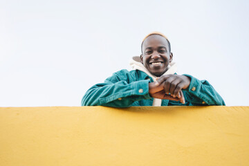 Friendly Young African Man looking to the camera from above yellow wall