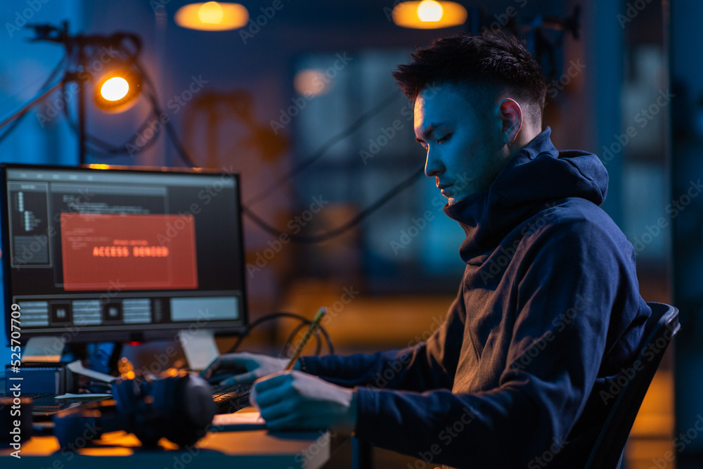 Poster cybercrime, hacking and technology concept - male hacker in dark room writing to notebook and using 