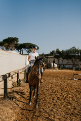 vertical photo of a young woman warming up with her brown horse in the riding arena
