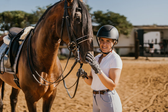portrait of young woman in riding attire posing with horse before dressage with helmet