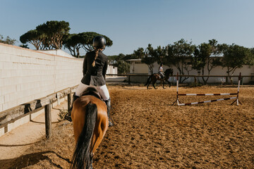 rear view of a woman in equestrian attire warming up a horse by circling the equestrian arena.