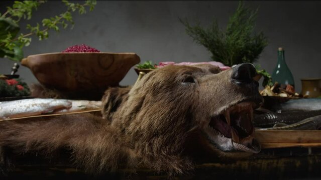 Large wooden table with food and drinks decorated with bear skin and head. Game meat and fish, wild berries