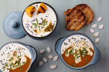 Creamy pumpkin soup with cream, black cumin seeds, herbs, pumpkin seeds and toasted bread on a blue wooden table