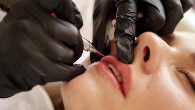 Permanent makeup procedure applying rose red pigment using tattoo machine in beautician salon. Microblading tattoo lips