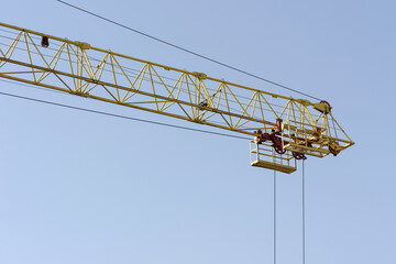 Tower crane at the construction site. Yellow boom crane with a winch against the blue sky. Element of a construction machine close-up. The concept of urban development and construction work.