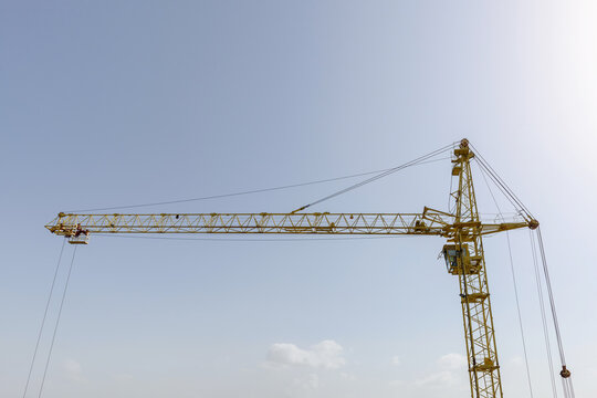 Tower crane at the construction site. Yellow boom crane with a winch against the blue sky. Construction machine element with place for text. The concept of urban development and construction work.