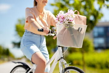 people, leisure and lifestyle - close up of woman with flowers and bag in basket of bicycle on city...