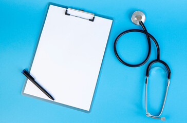 Stethoscope and clipboard with blank white sheet of paper and pen, on blue background. Place for text.