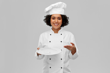 cooking, culinary and people concept - happy smiling female chef in white toque and jacket holding empty plate over grey background