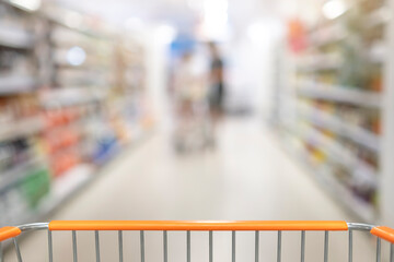 Blurred supermarket aisle with shelves of merchandise and a shopping cart in the foreground -