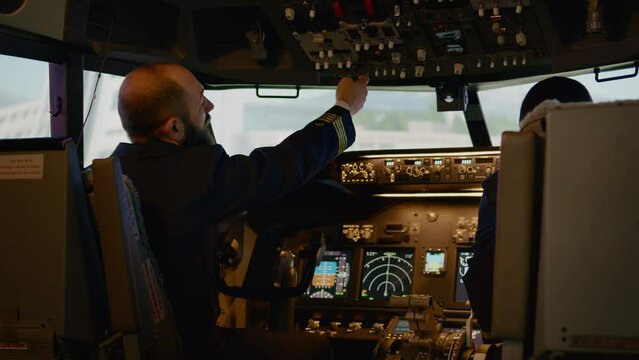 Diverse captain and copilot switching power buttons to fly airplane, preparing to takeoff with engine command. Using control panel and cockpit dashboard for airline transport. Handheld shot.