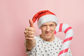 Mature cheerful man looking at the camera on a pink background. Smiling elderly guy in a santa hat