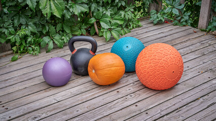 three heavy slam balls, iron kettlebell and pumpkin on a backyard deck, home and backyard gym...