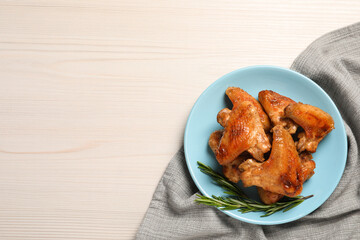 Plate with delicious fried chicken wings and sprig of rosemary on white wooden table, top view. Space for text