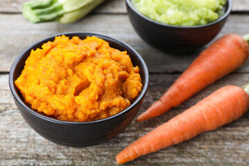 Tasty puree in bowls, zucchini and carrots on wooden table, closeup